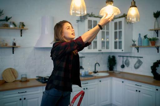 A woman changing a light bulb in a house.