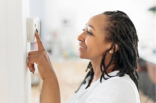 A woman adjusting a thermostat in a home.